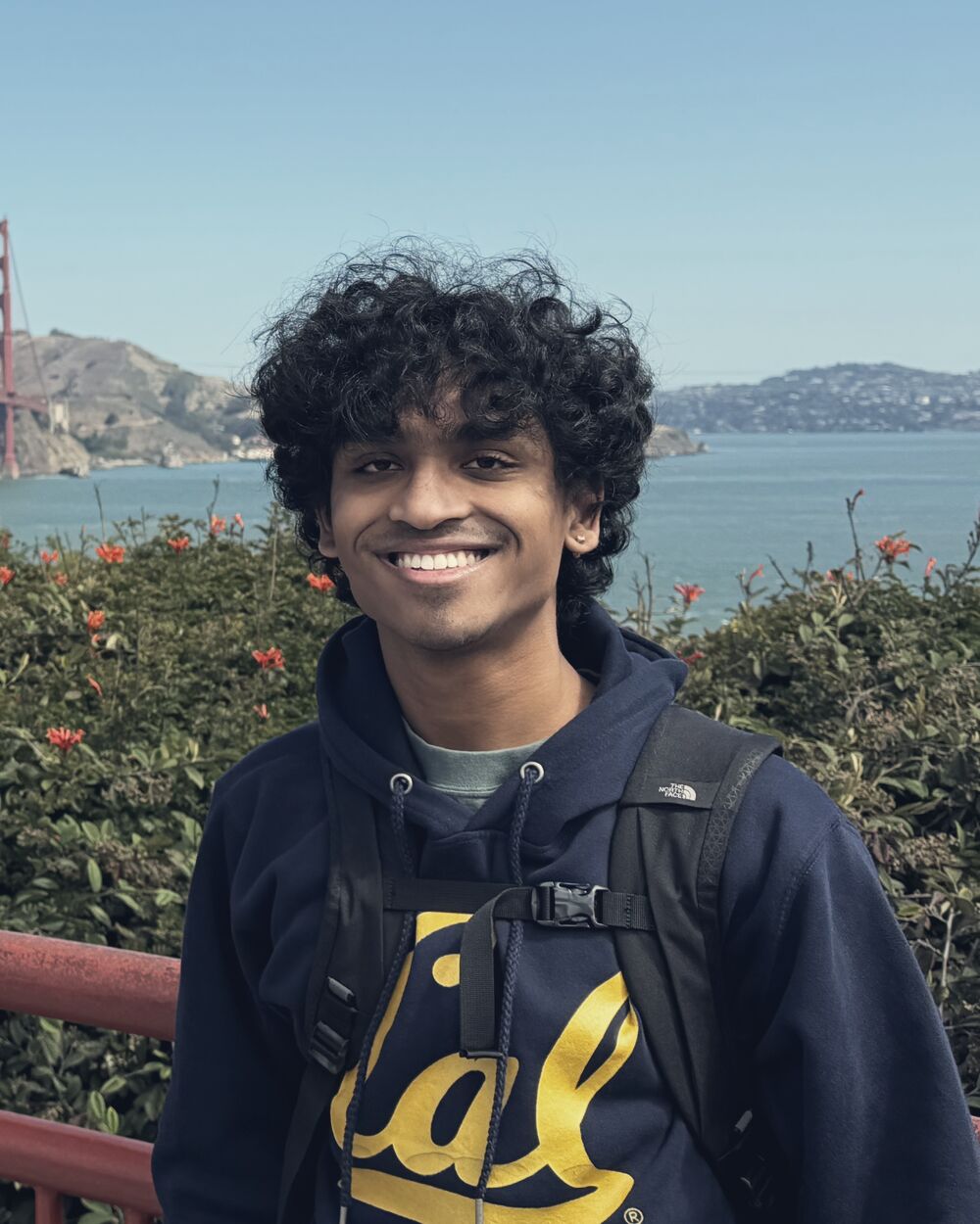 Arnav in a Cal hoodie, smiling, with the bay behind him