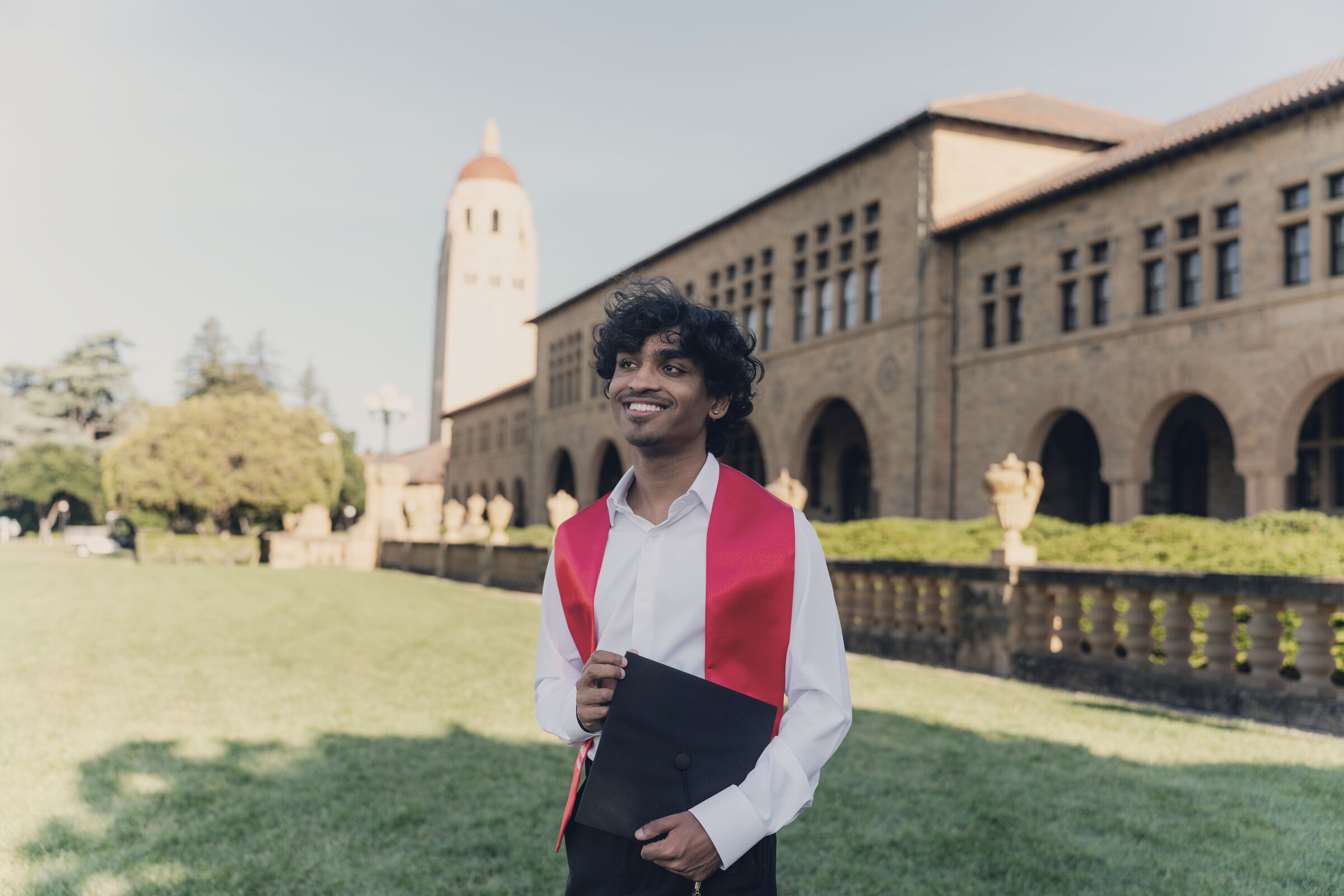 Arnav in his graduation stole on a sandstone campus, a bell tower behind him